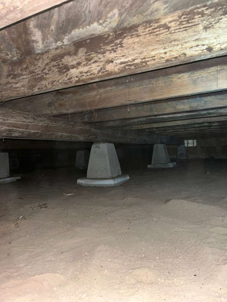 Interior view of a pier and beam foundation crawl space in FortWorth and Grapevine, TX, showing concrete piers and wooden joists, inspected by Brown Foundation Repair.