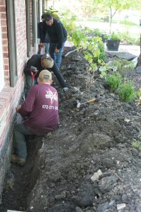Brown Foundation Crew digging trench along home foundation to install Hydraway drainage system for improved water management.