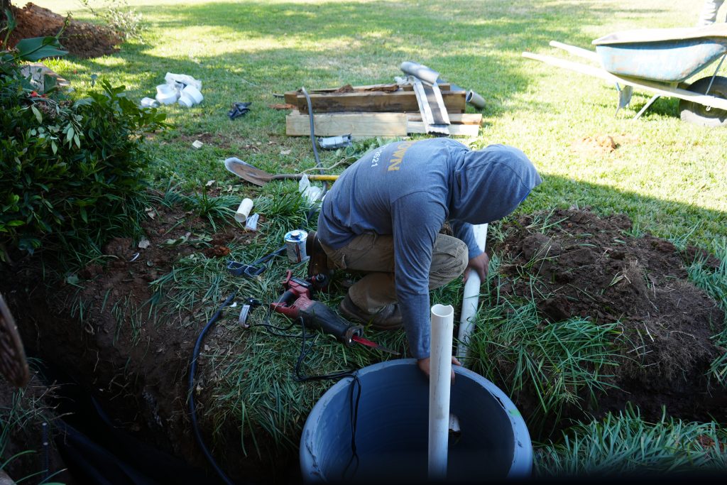 Hydraway drain system installation with worker placing PVC pipe into drainage basin for foundation waterproofing.