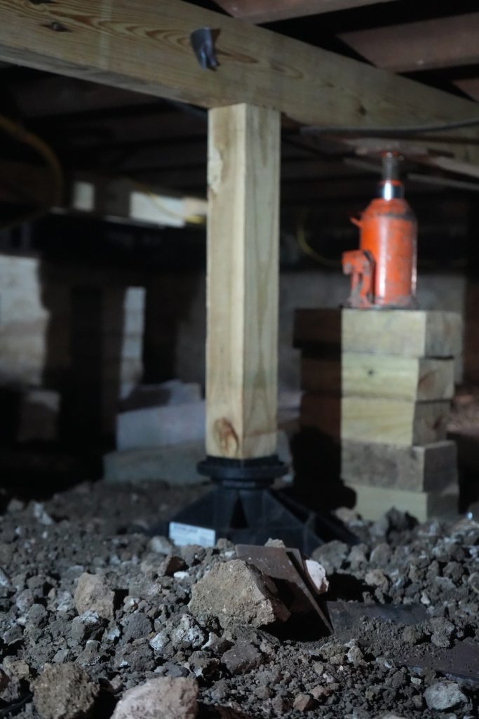 Crawl space support post installed with jacks and shims during pier and beam stabilization.