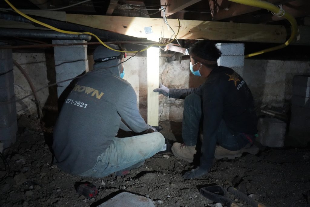 Brown Fondation Technicians performing crawl space adjustment and leveling under pier and beam home.