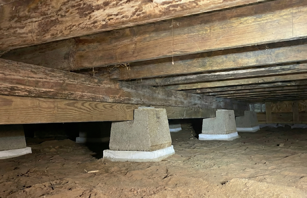 New concrete cinder block piers sitting on reinforced support pads in a crawl space, supporting wooden floor beams.